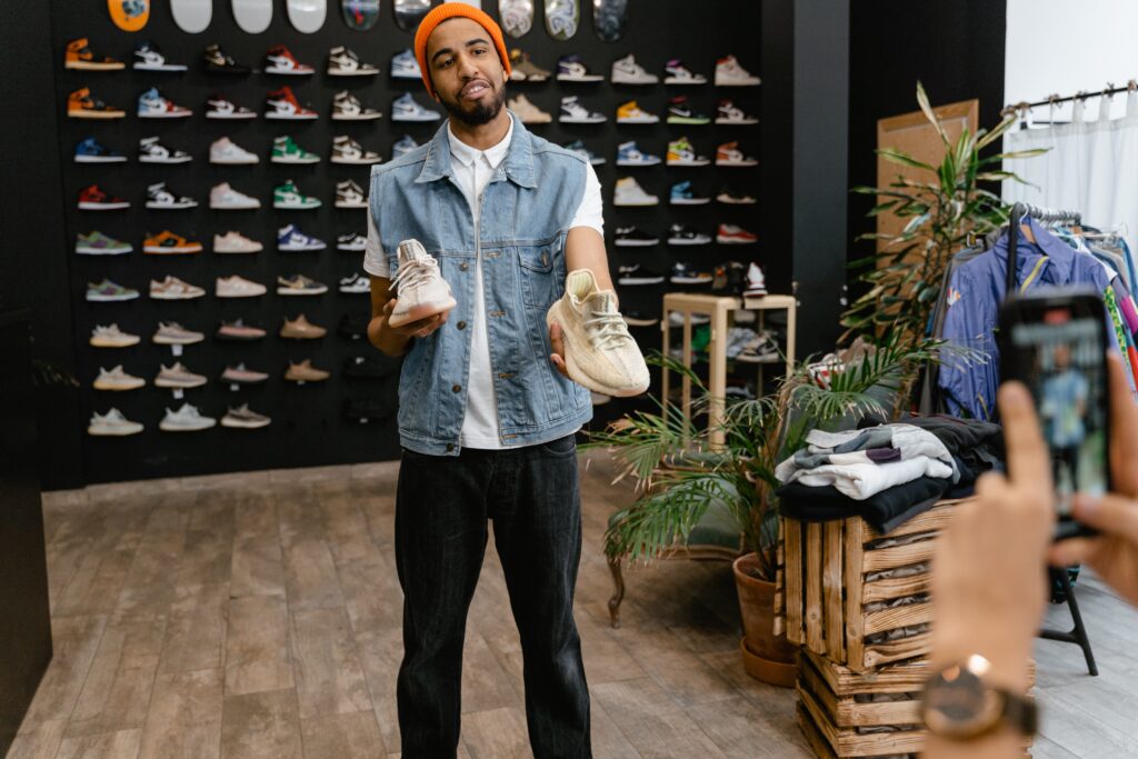 A man holding shoes in his hands while selling in front of a camera